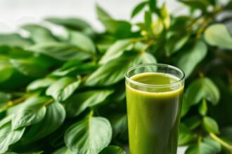 Un gros plan de feuilles de moringa vibrantes avec un arrière-plan flou, accompagné d'un petit bol de poudre de moringa et d'un verre de smoothie v...